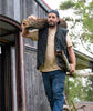 Man wearing Volcom vest over tan tee and navy cargo pants carrying firewood outside cabin, autumn streetwear style